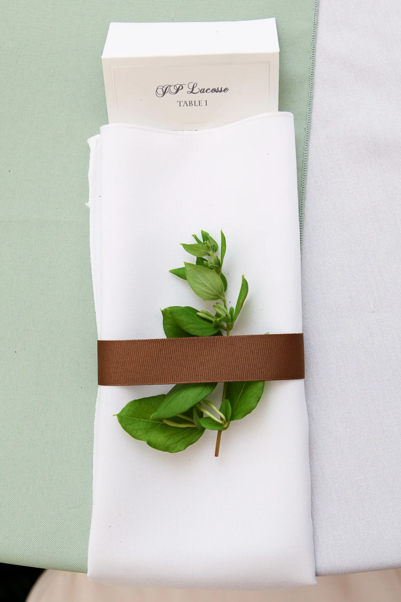 A white napkin wrapped in a brown band and a single green leaf, printed menu above