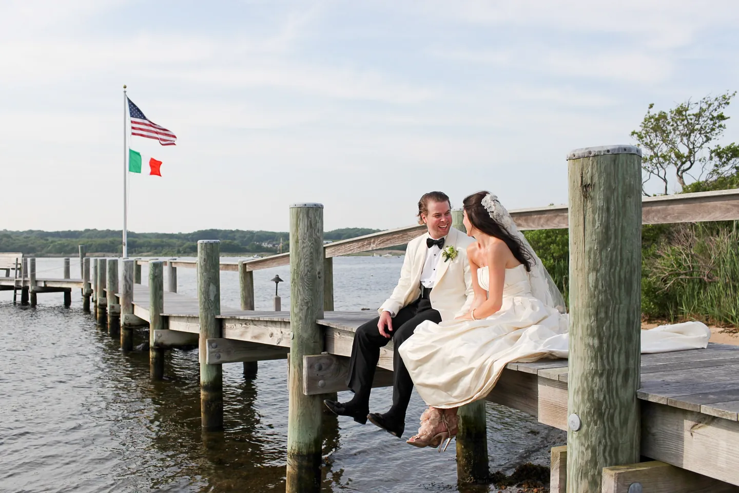 Kaitlin and Matthew sit on the edge of a wooden dock under American and Italian flags