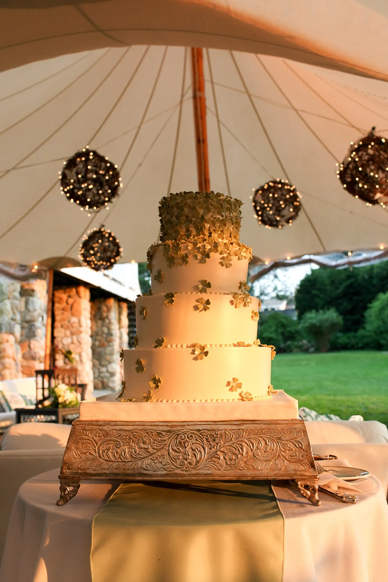 A tall tiered wedding cake under the peak of a sailcloth tent with hanging lanterns