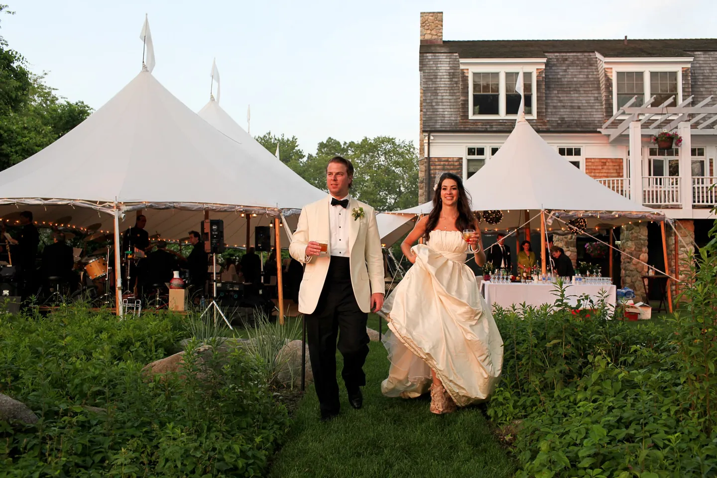 Kaitlin and Matthew walk a garden path away from the sailcloth tents, the shingled house behind