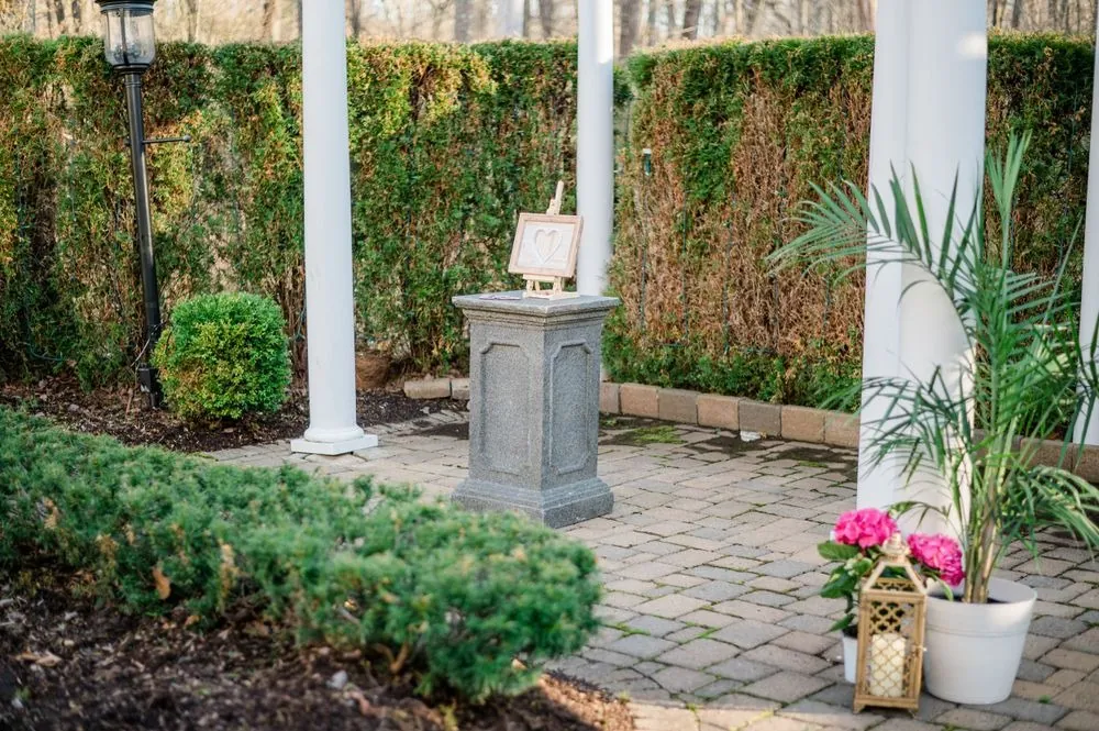 The ceremony site under a white pergola with potted palms, hedges and a stone pedestal