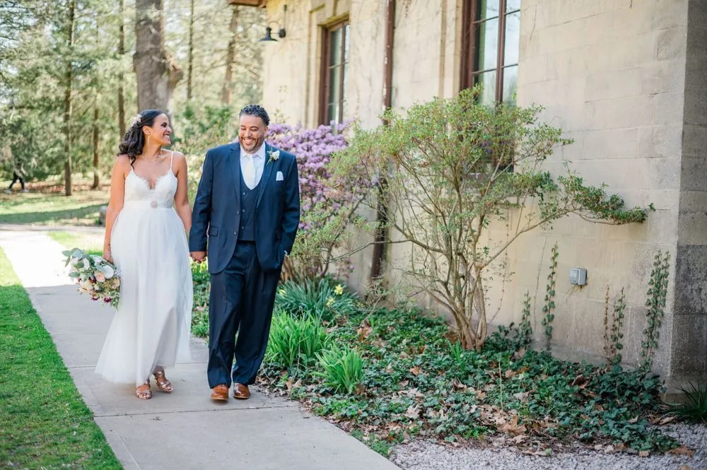 Karla and Carlos stroll a garden walk lined with azaleas beside the stone building