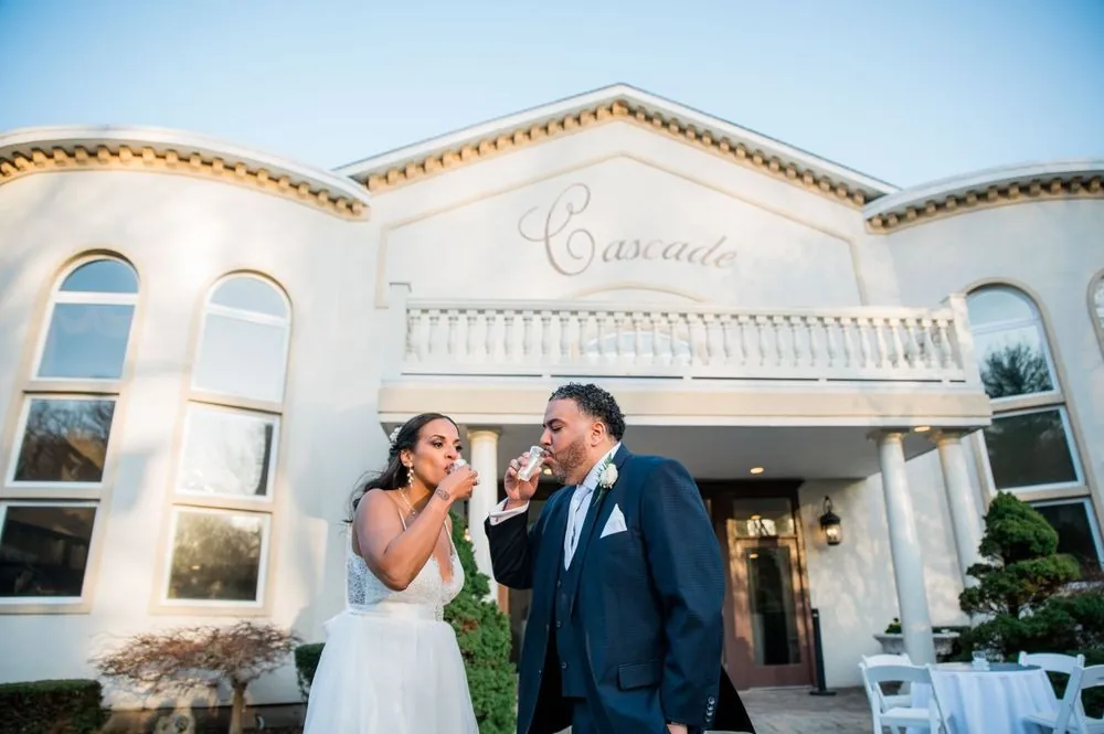 Karla and Carlos raise small glasses together on the front steps below the Cascade sign