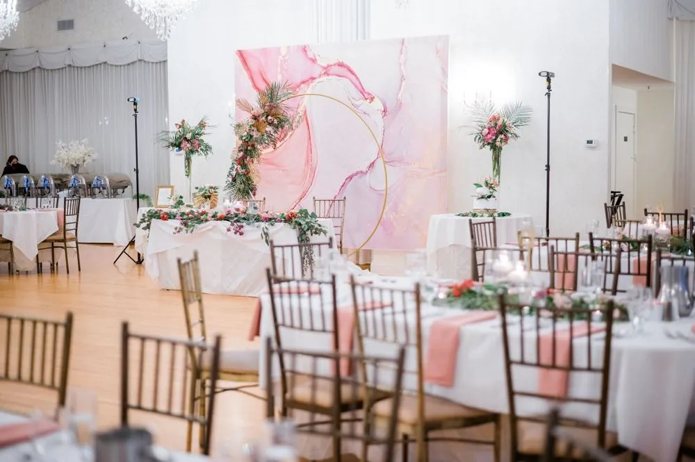 The reception room set with blush linens, gold chairs and a pink marbled backdrop