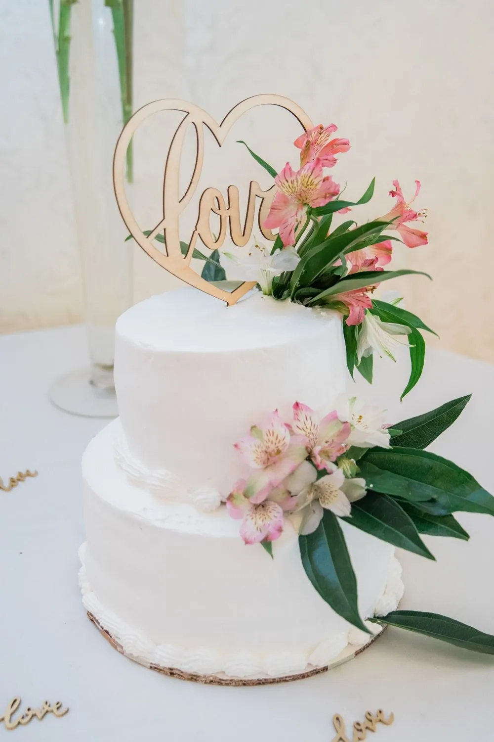 A 2-tier white cake with pink blooms and a gold script topper