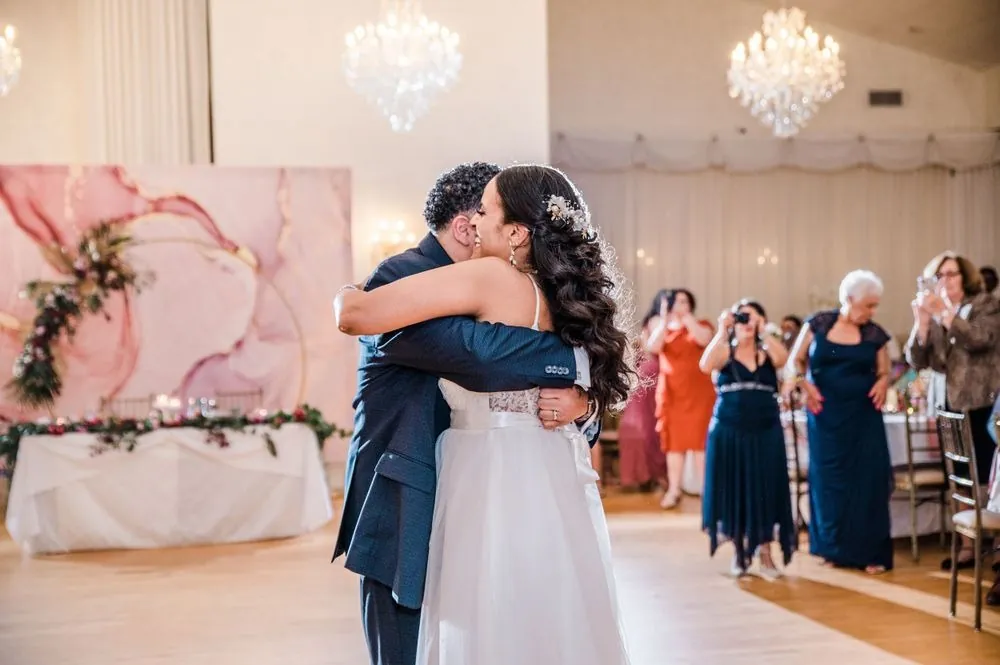 Karla and Carlos hug on the dance floor under crystal chandeliers as guests take photos