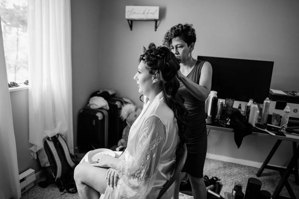 Black and white of a stylist pinning the bride's hair beside the bedroom window