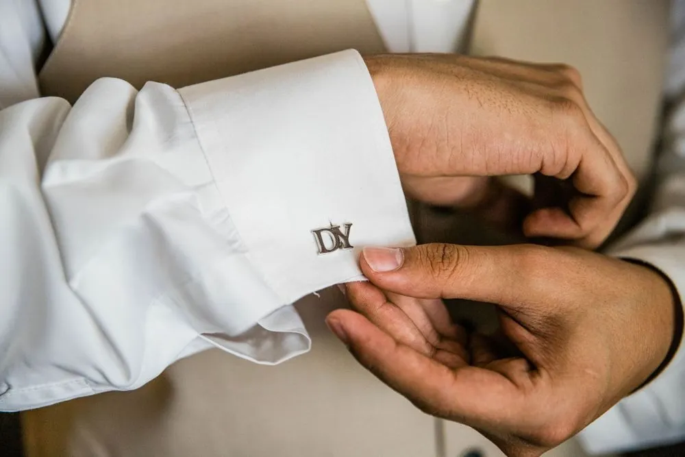 Close view of hands fastening a cufflink engraved with the couple's initials
