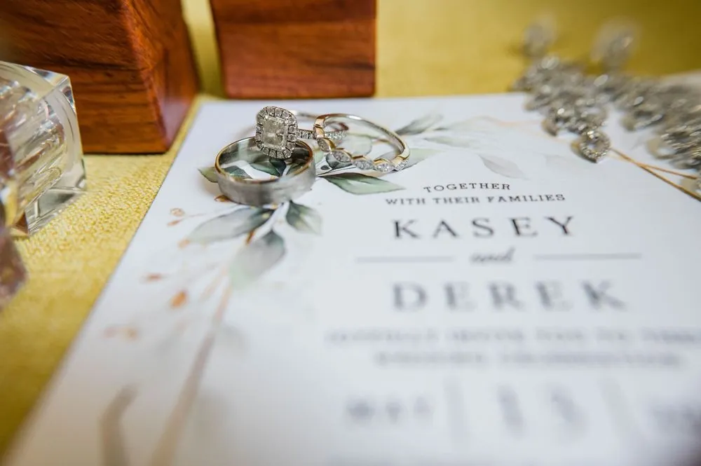 Wedding invitation with greenery watercolor and gold rings on a wood surface