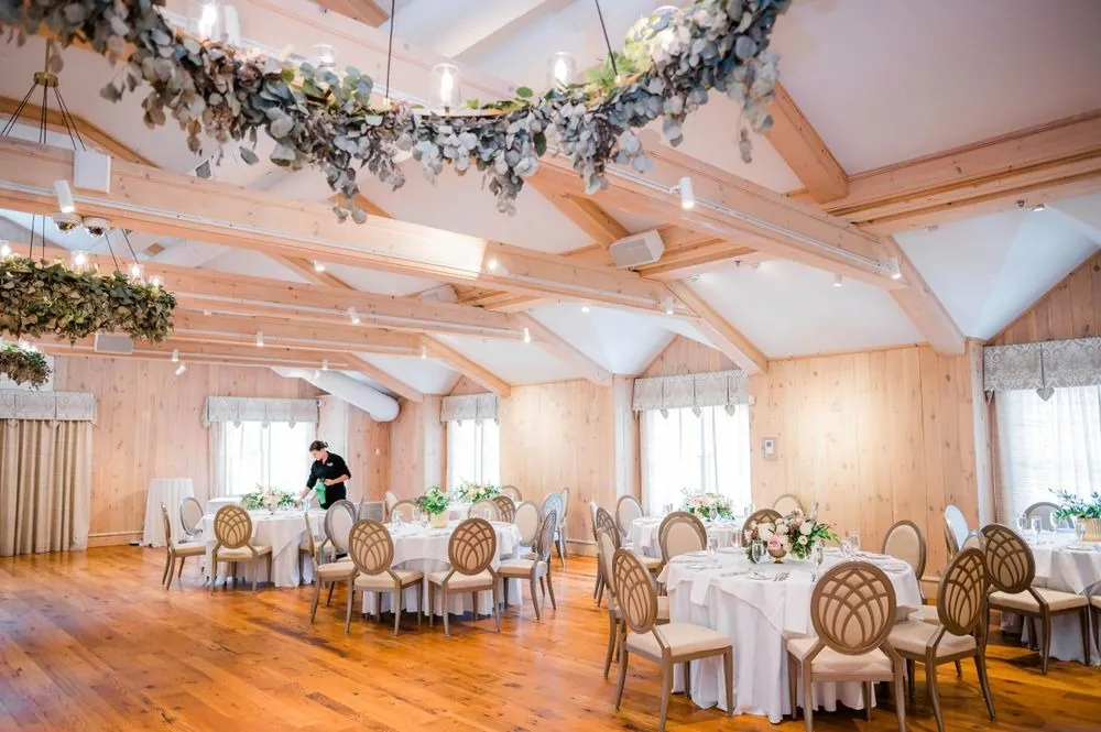 Reception hall with wood floors, round tables and greenery hoops hanging overhead
