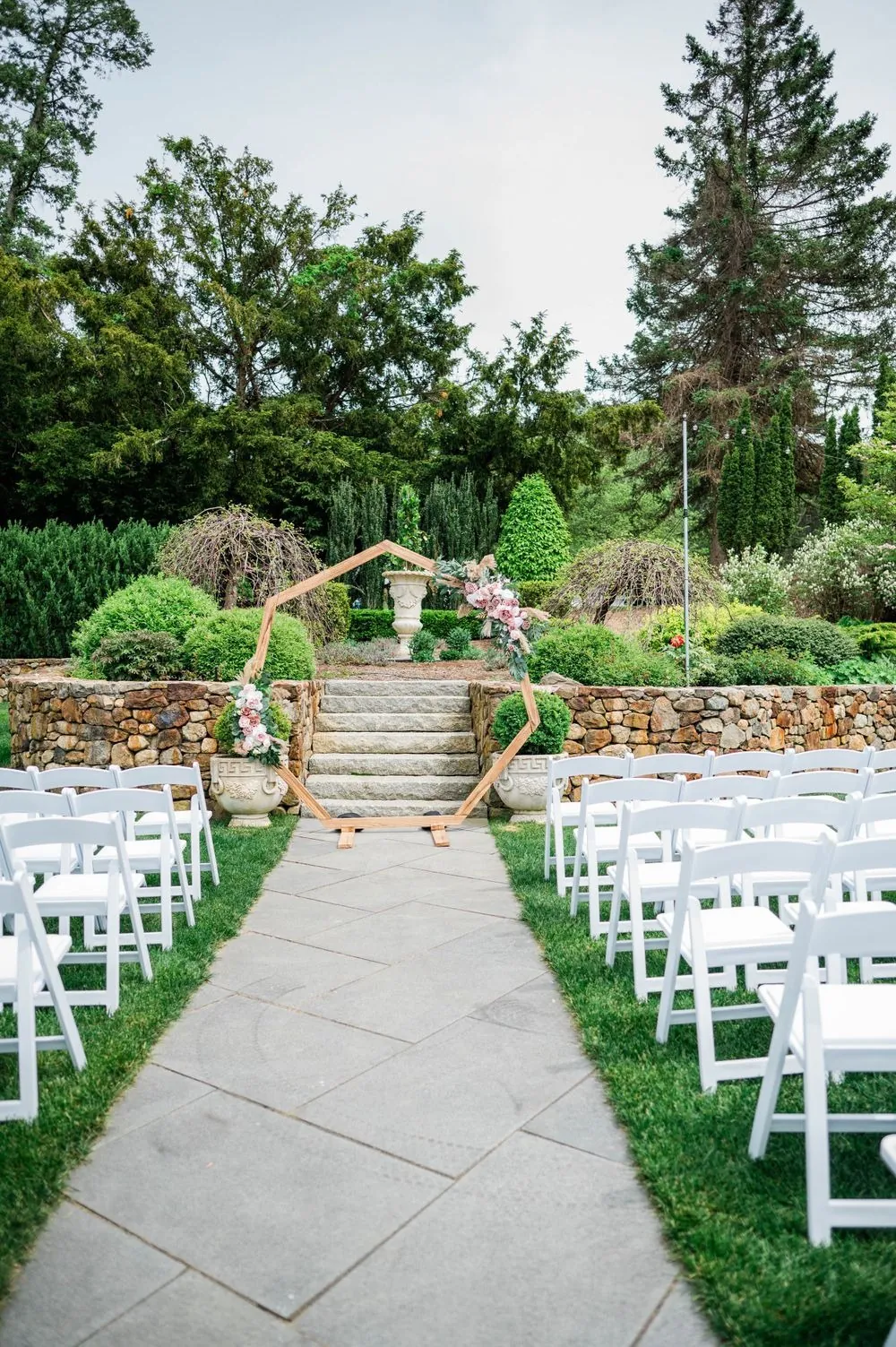 Rows of white chairs line a stone path through the garden ceremony site