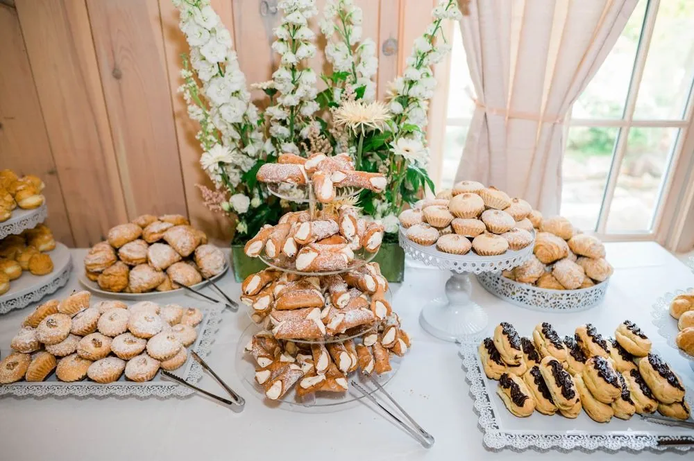 A dessert table crowded with cookies and pastries among pale flowers