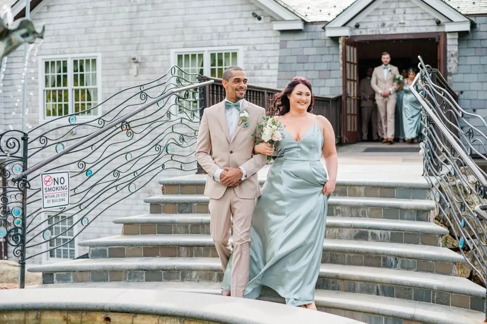 A bridesmaid in sage satin walks down the curving stone staircase
