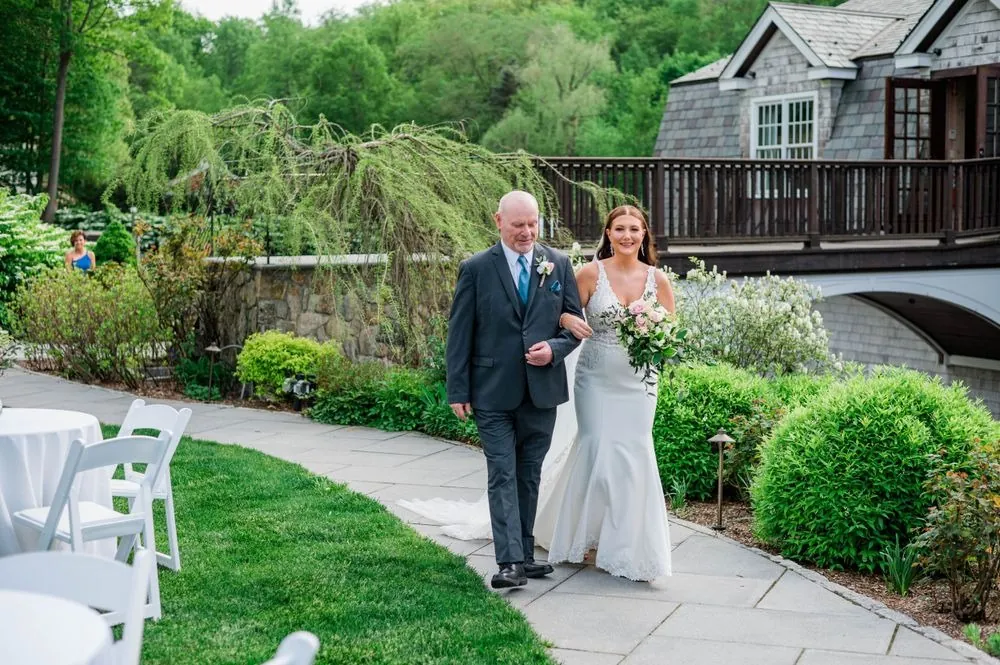 The bride walks the garden path with an older man in a charcoal suit