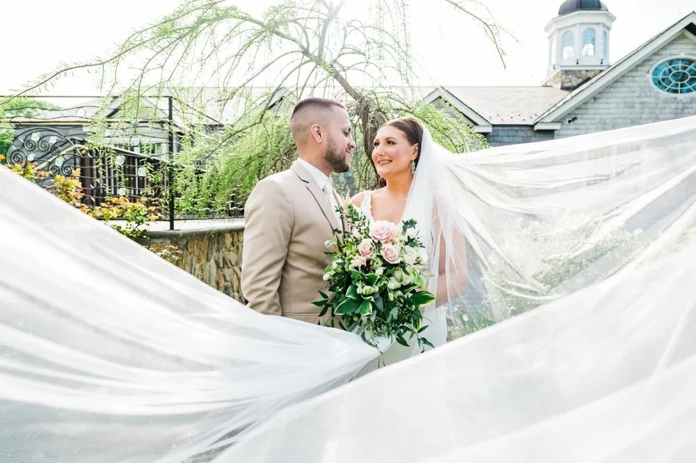 Kasey and Derek smile at each other as her cathedral veil sweeps around them