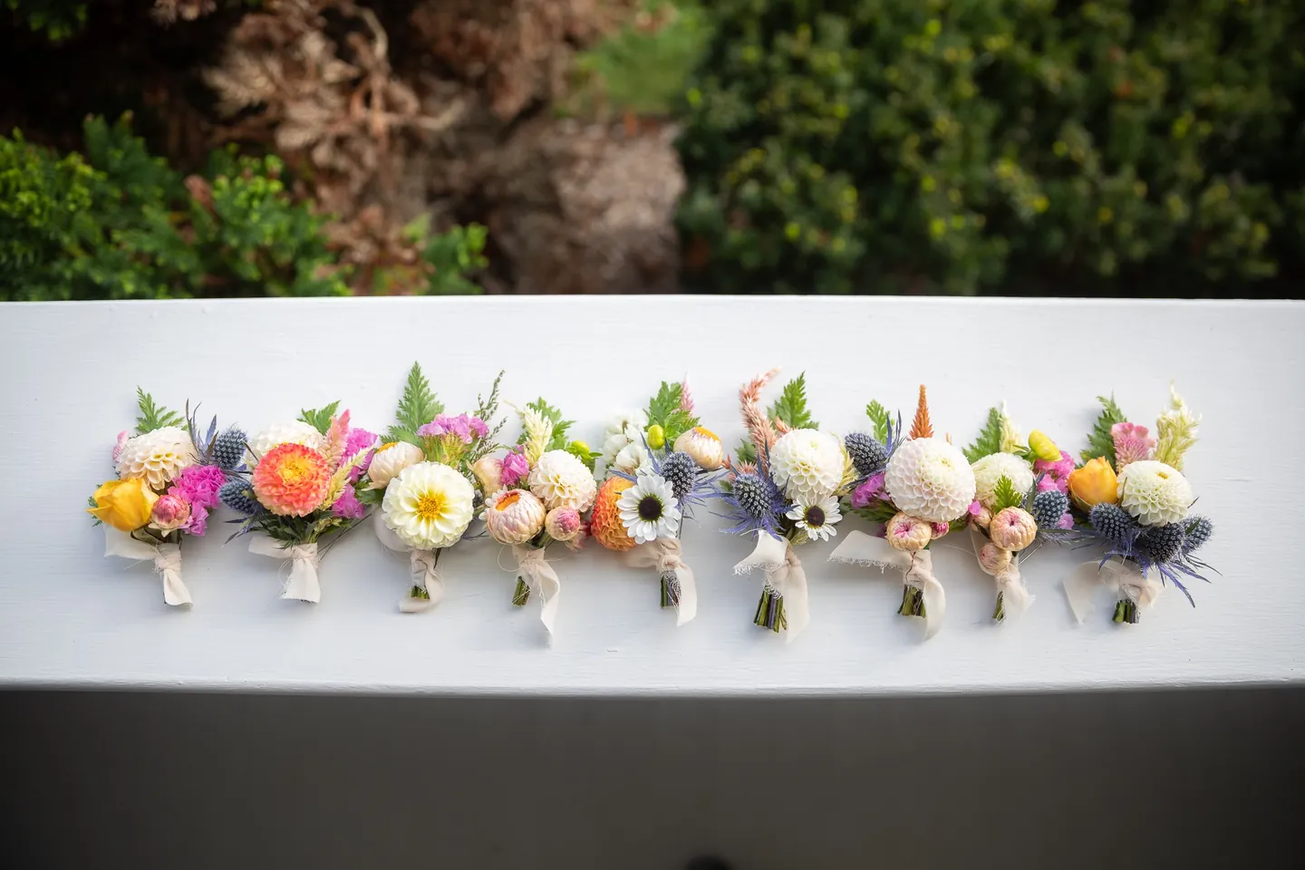 A row of dahlia and ranunculus boutonnieres lined up on a white windowsill