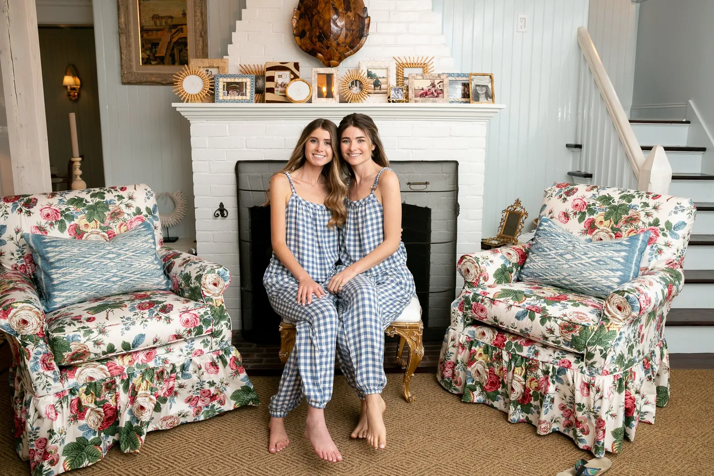 Two bridesmaids in blue sit by a white fireplace between floral armchairs