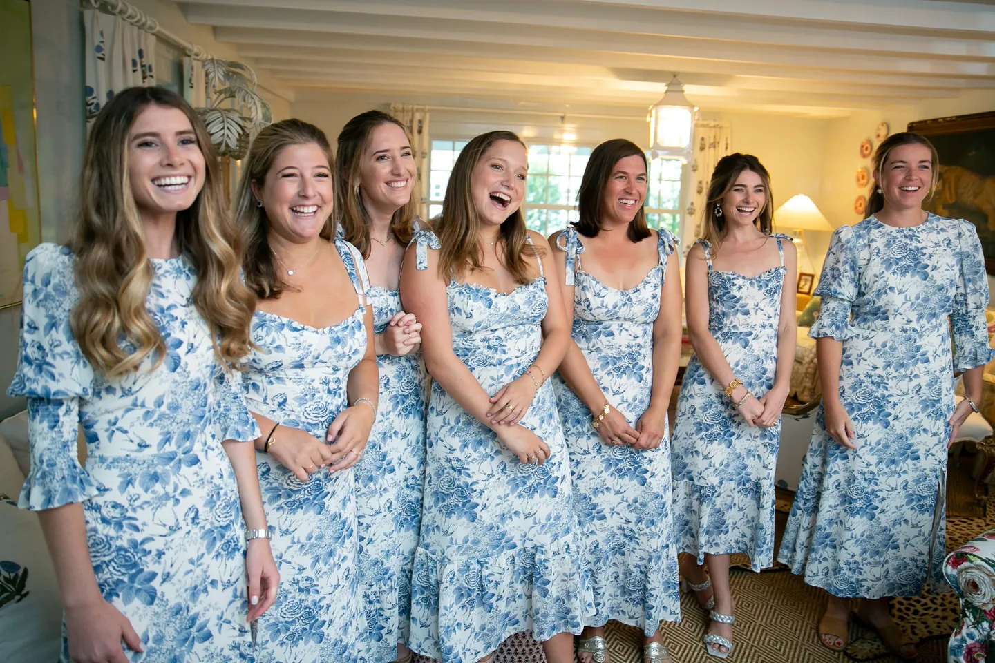 Bridesmaids in matching blue and white toile dresses laugh together in a sunny room