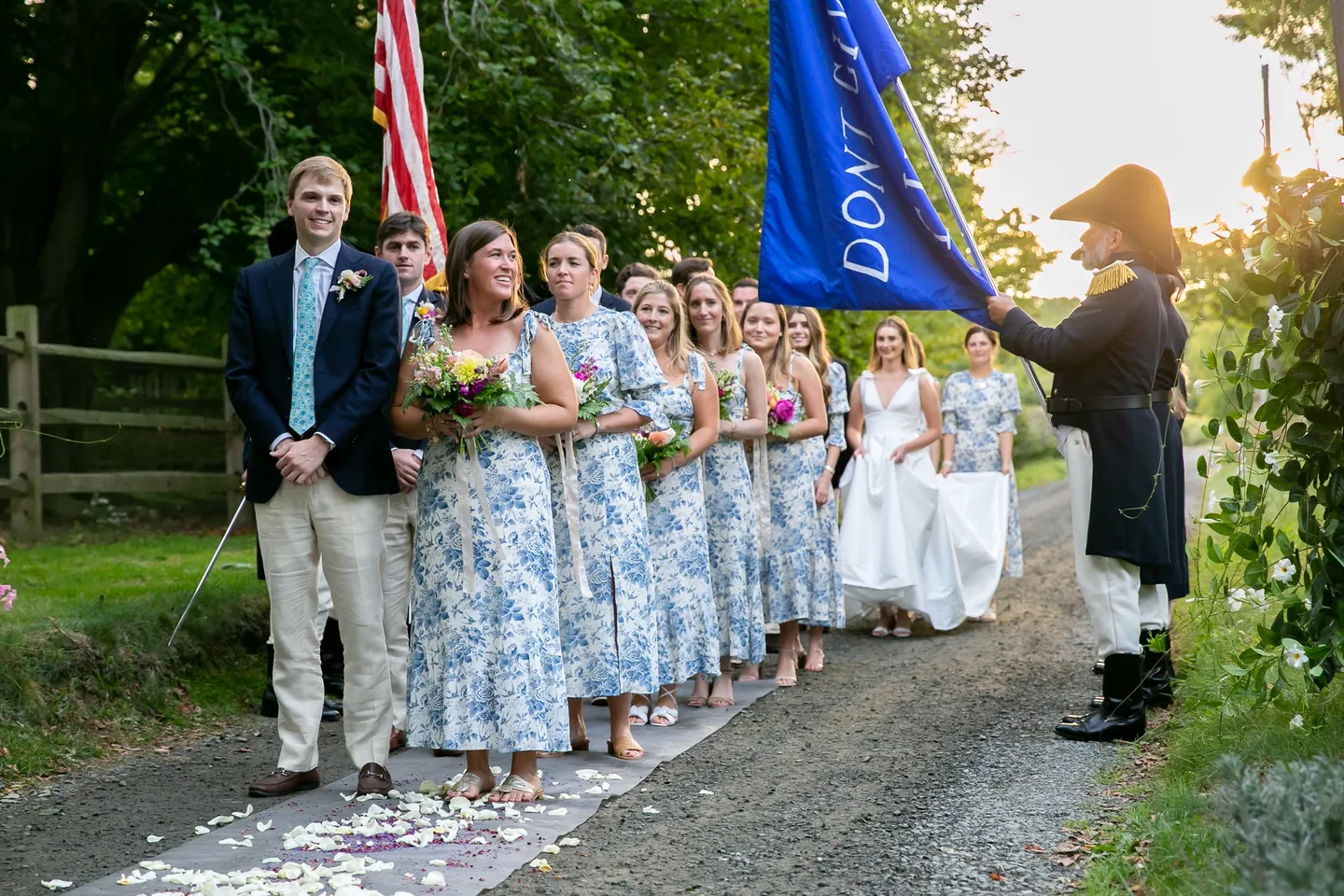 The wedding party stands along the lane in toile and navy as a corps member carries a blue flag