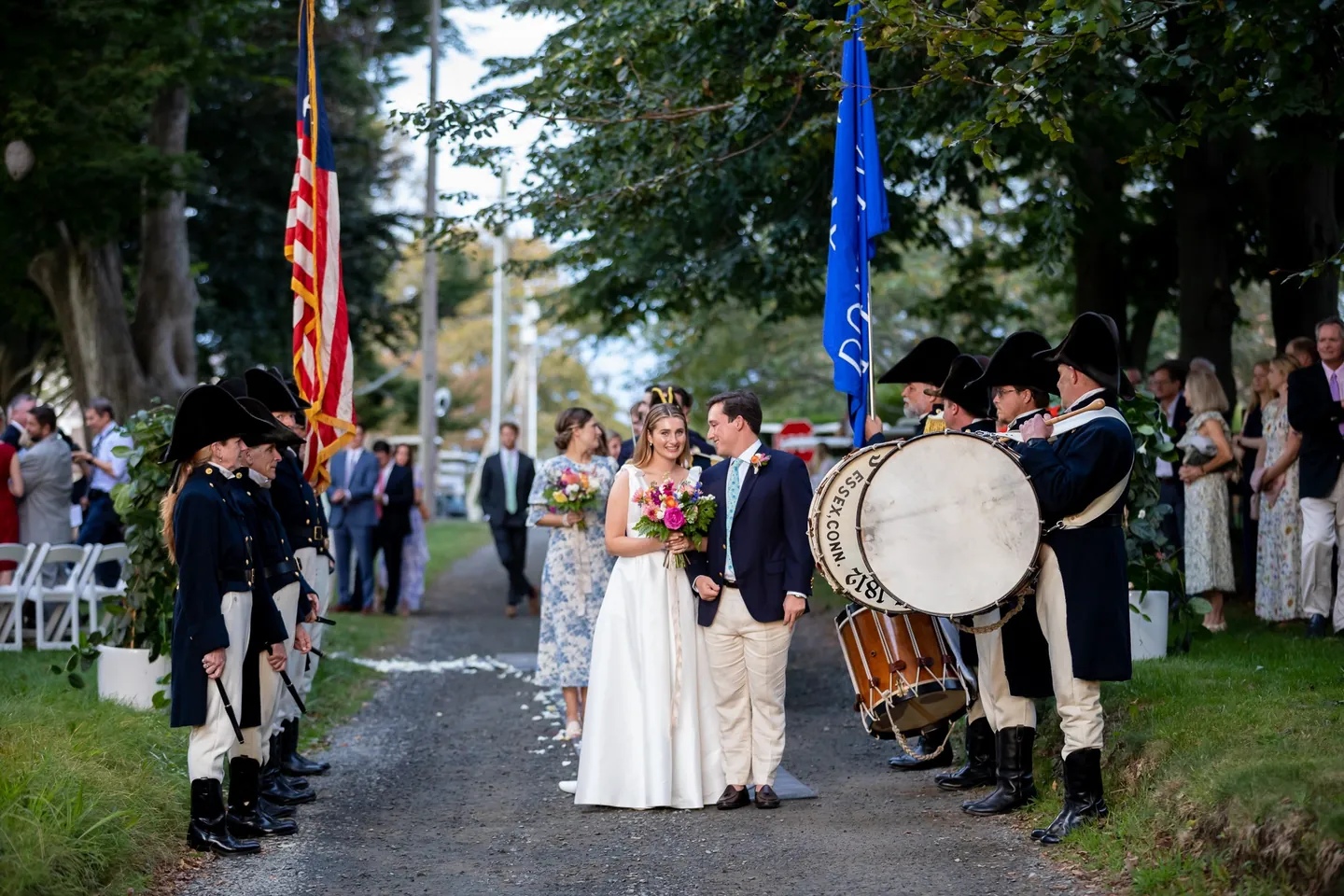 Kate and Parker stand between rows of fifers and drummers on a petal-strewn lane