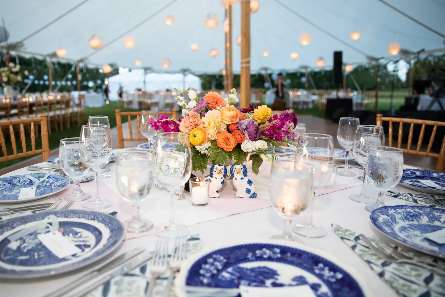 A round table set with blue and white china and bright flowers under the tent