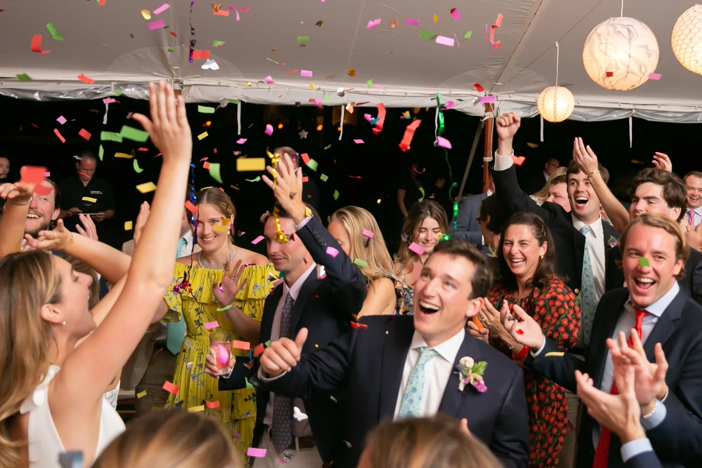 Confetti rains over a crowd of guests cheering on the tent dance floor