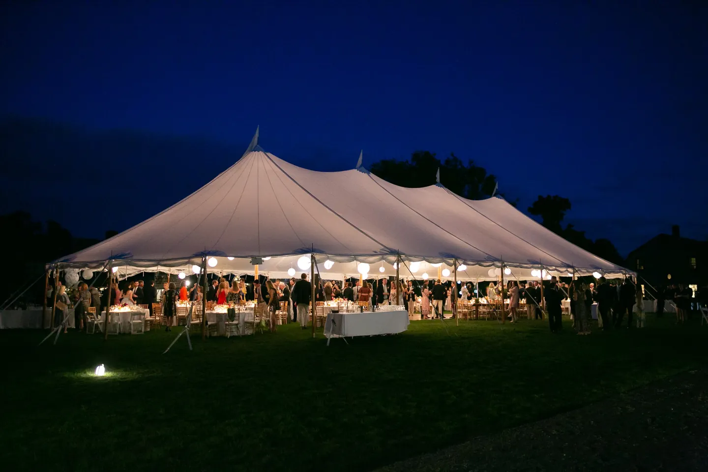 The sailcloth tent glows on a dark lawn under a deep blue night sky