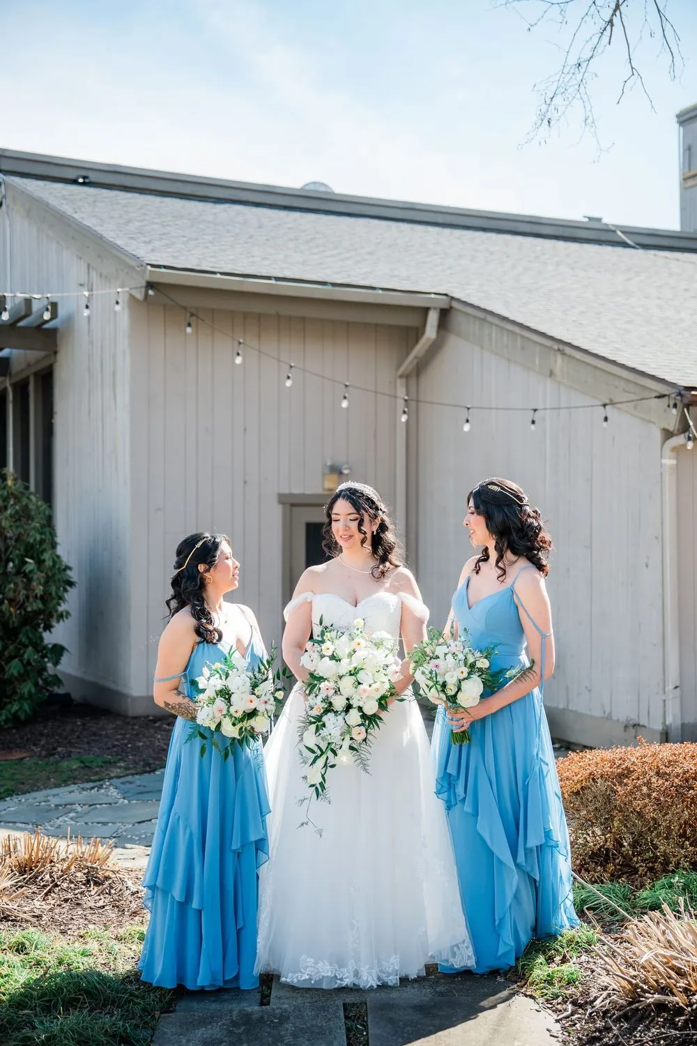 The bride between two bridesmaids in soft blue dresses holding white rose bouquets
