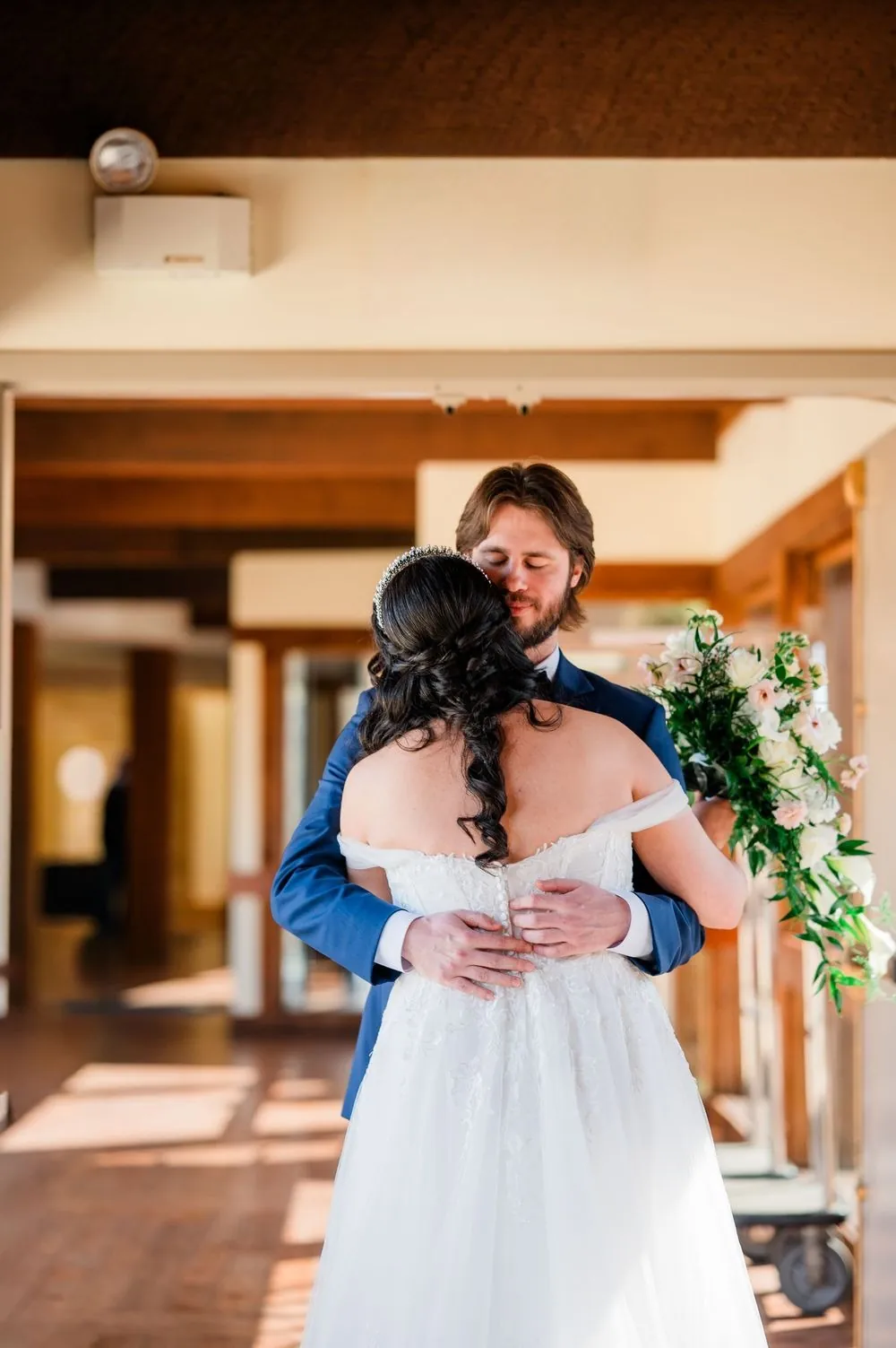 Monica and Kevin embrace beside a tall window in the hotel's wood-trimmed lobby