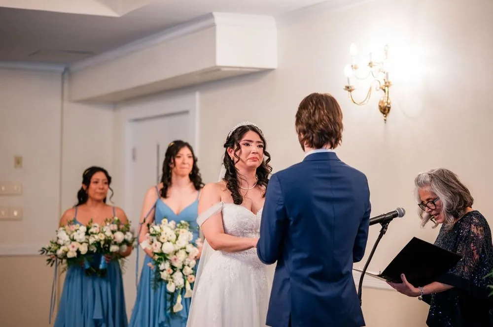 The bride fights tears during the vows as the officiant reads beside a brass sconce