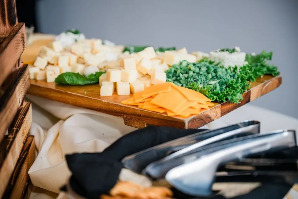 Cocktail hour cheese board with cubed cheeses and greens on a wood tray