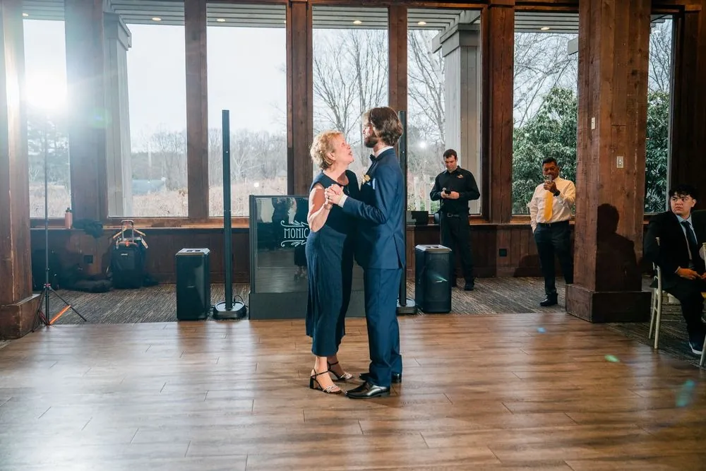 The groom slow dances with a woman in navy in front of the hall's tall windows