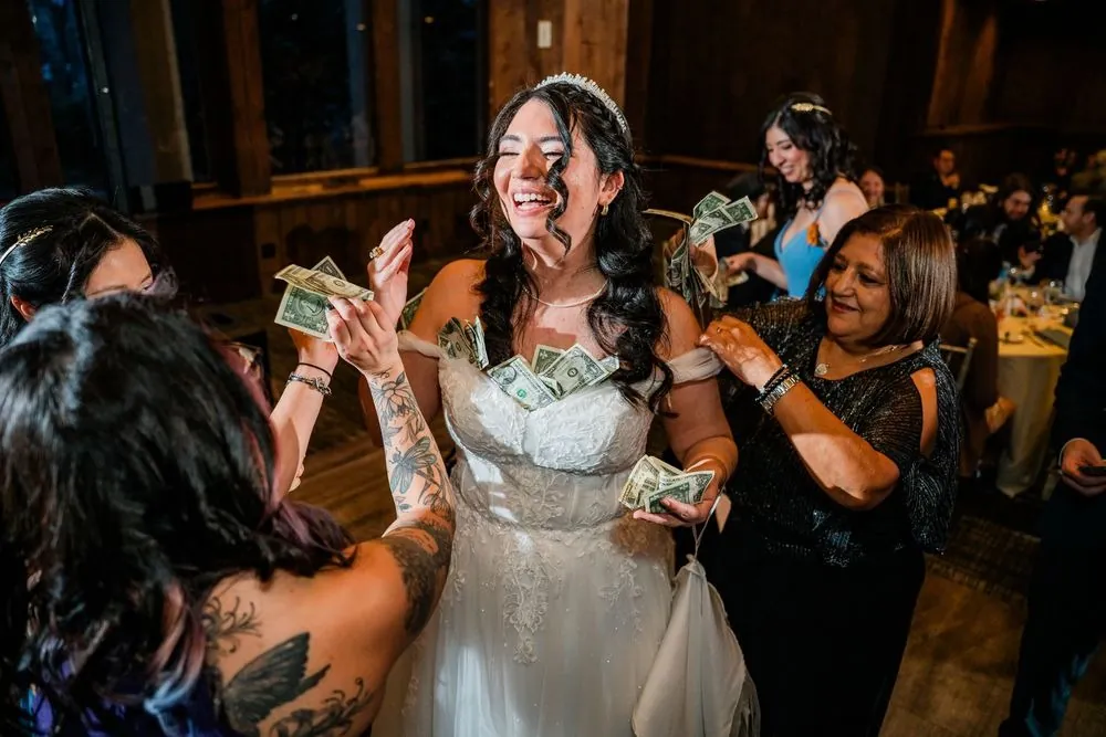 The bride laughs with dollar bills tucked into her gown during the Greek money dance