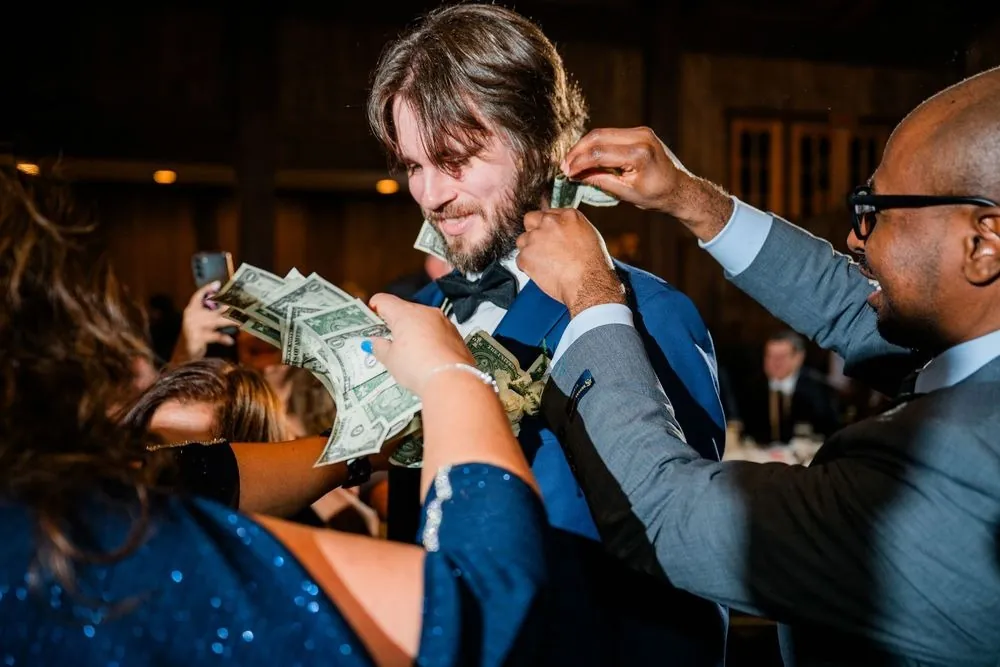 Guests tuck dollar bills into the groom's collar during the money dance