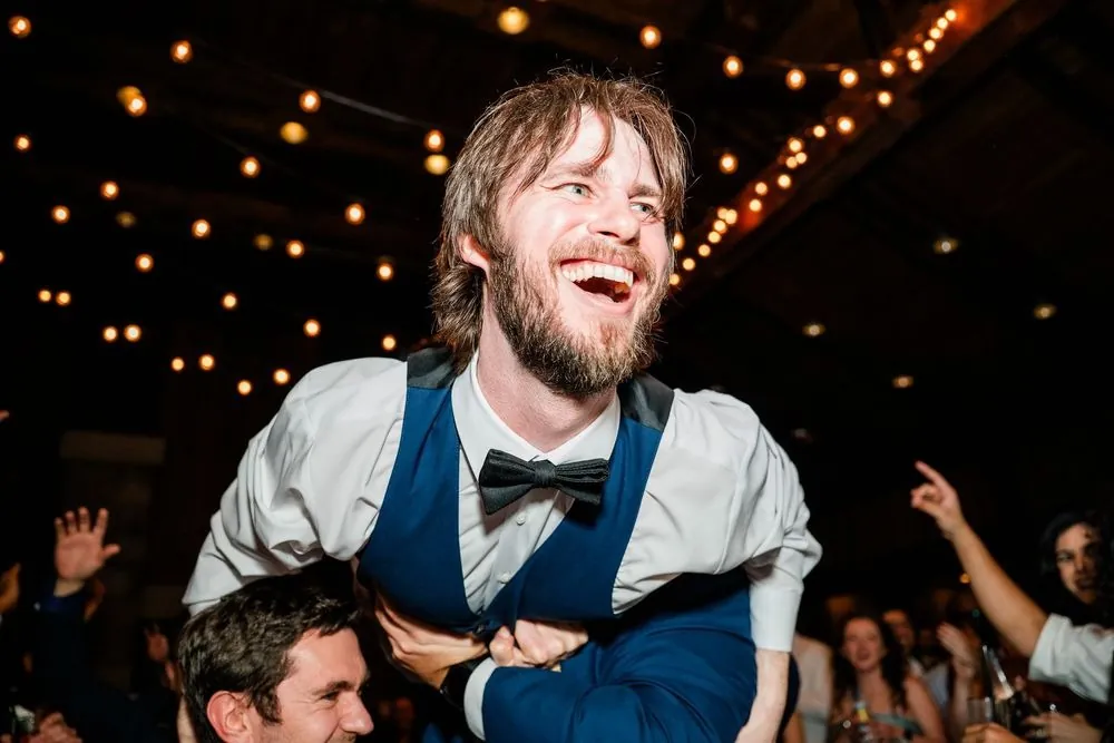 Close view of the groom grinning from his groomsmen's shoulders late in the night