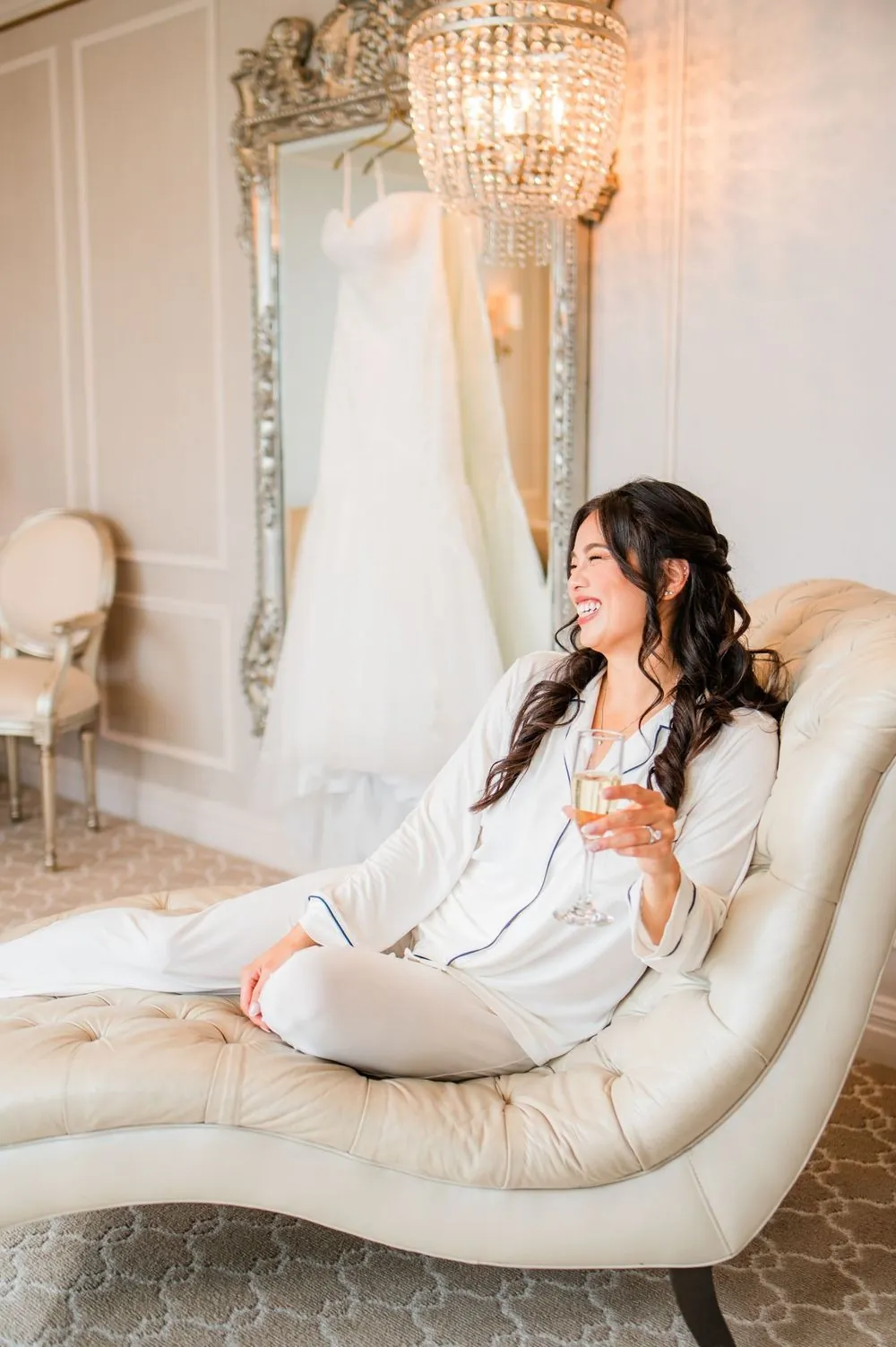 Bride in a white robe stretches out on a cream chaise in the bridal suite