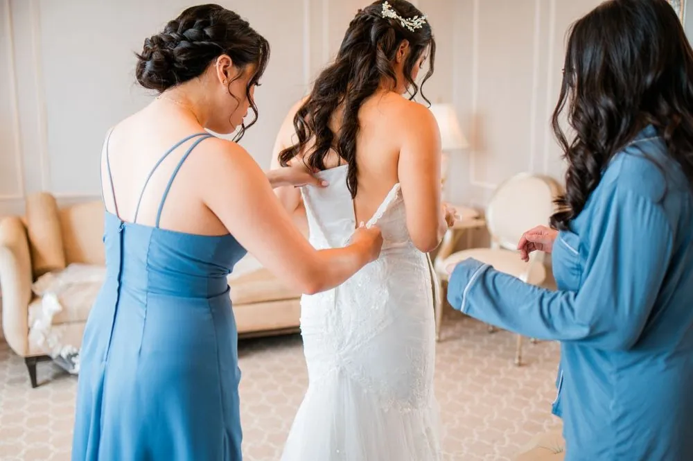 Bridesmaids in blue fasten the back of the bride's strapless gown