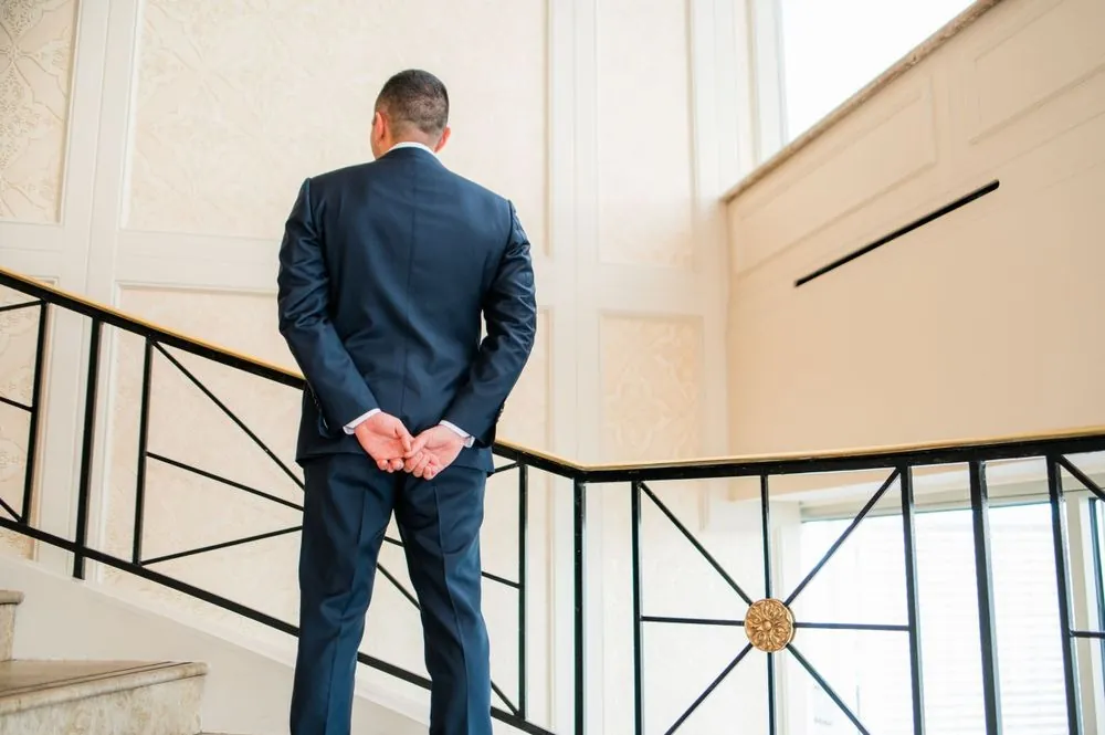Groom waits with his back turned at the rail of a curving staircase