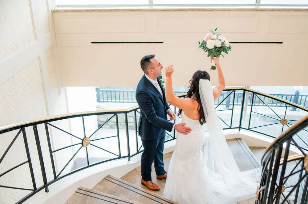 Kim raises her bouquet in the air as Fabiano turns to see her on the staircase