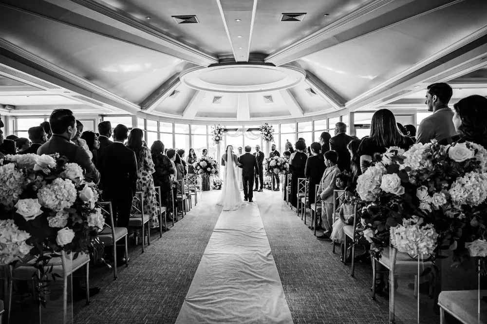 Black and white view down the aisle past rows of guests toward the windows