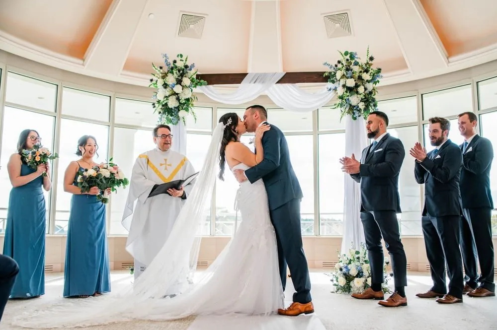Kim and Fabiano kiss under the draped arch as bridesmaids and groomsmen look on
