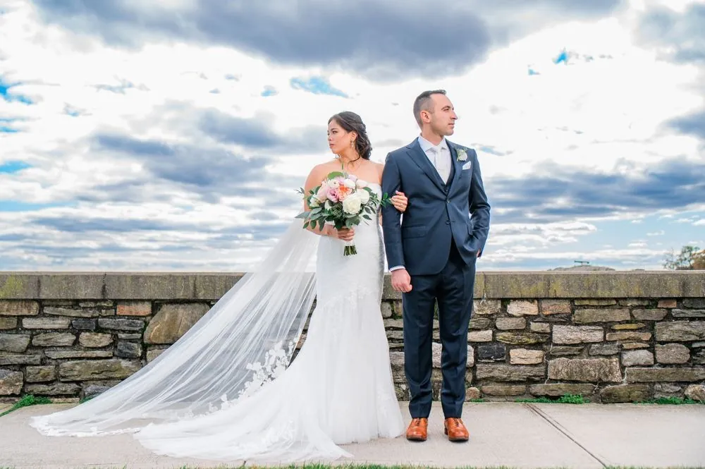 Kim and Fabiano stand at the stone seawall under a big cloudy sky