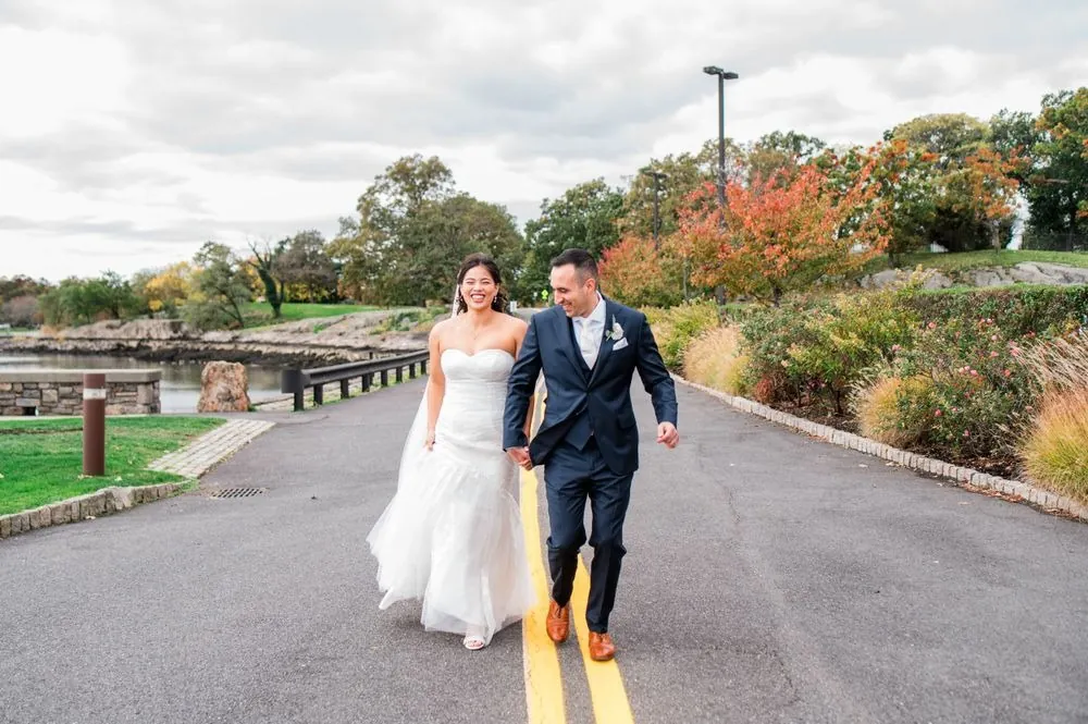 Kim and Fabiano walk up the drive laughing, orange fall trees along the road