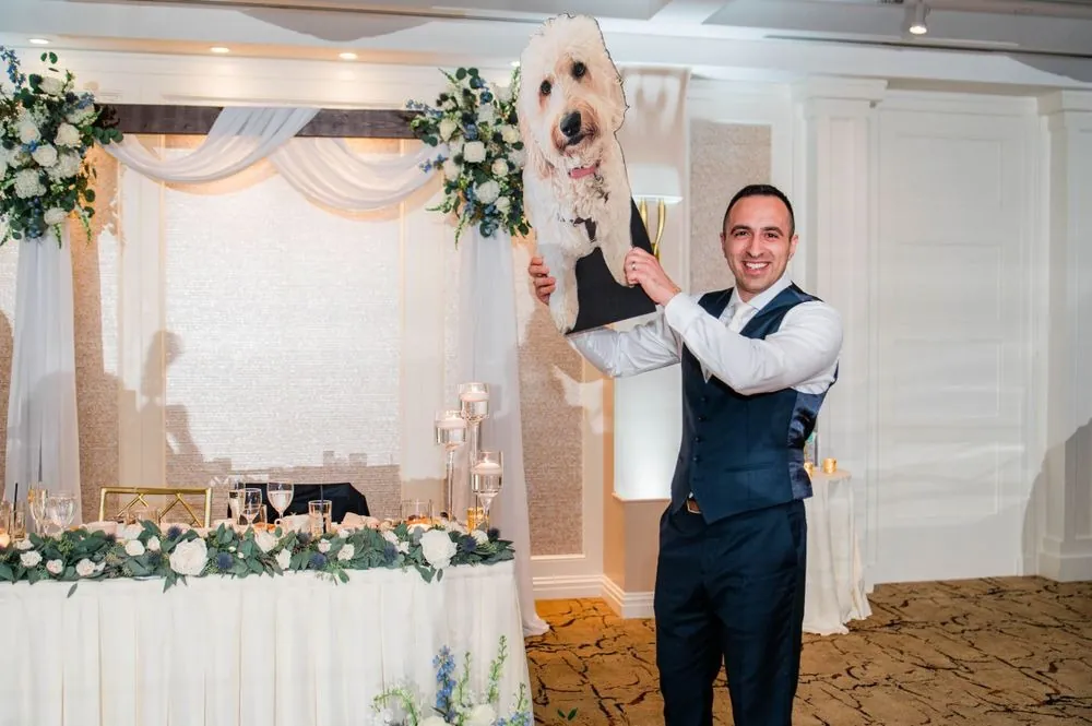 Groom lifts a cutout of the couple's goldendoodle high beside the head table