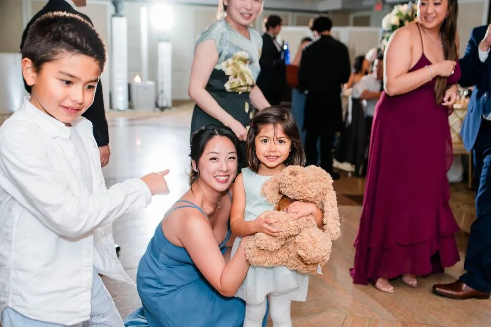 Guest crouches beside two kids holding teddy bears on the dance floor
