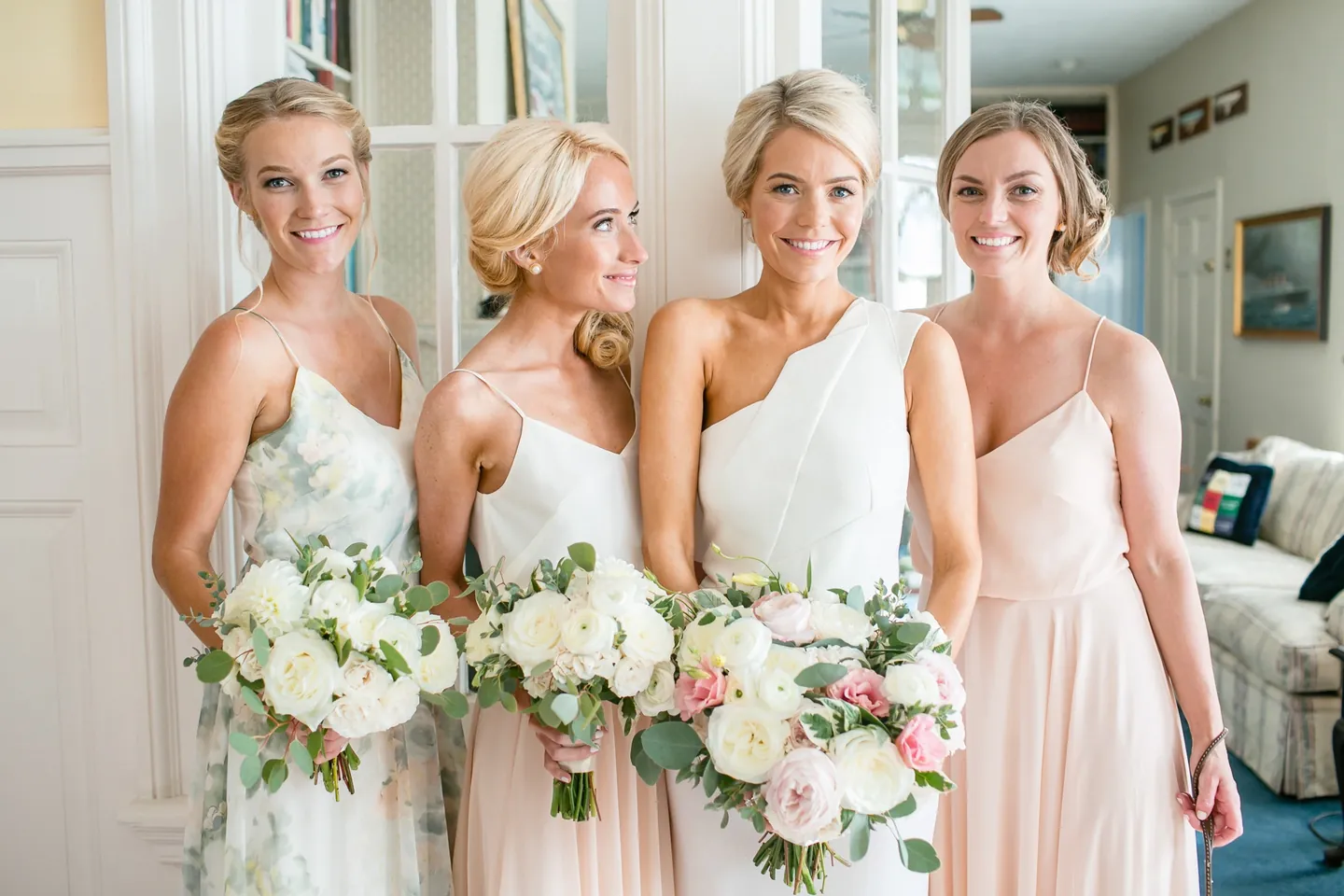 Bridesmaids in blush gowns and the bride hold white and pink bouquets side by side