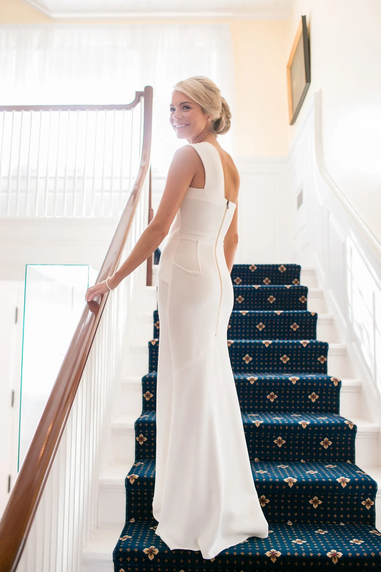 The bride walks down a staircase with a navy runner and white railings