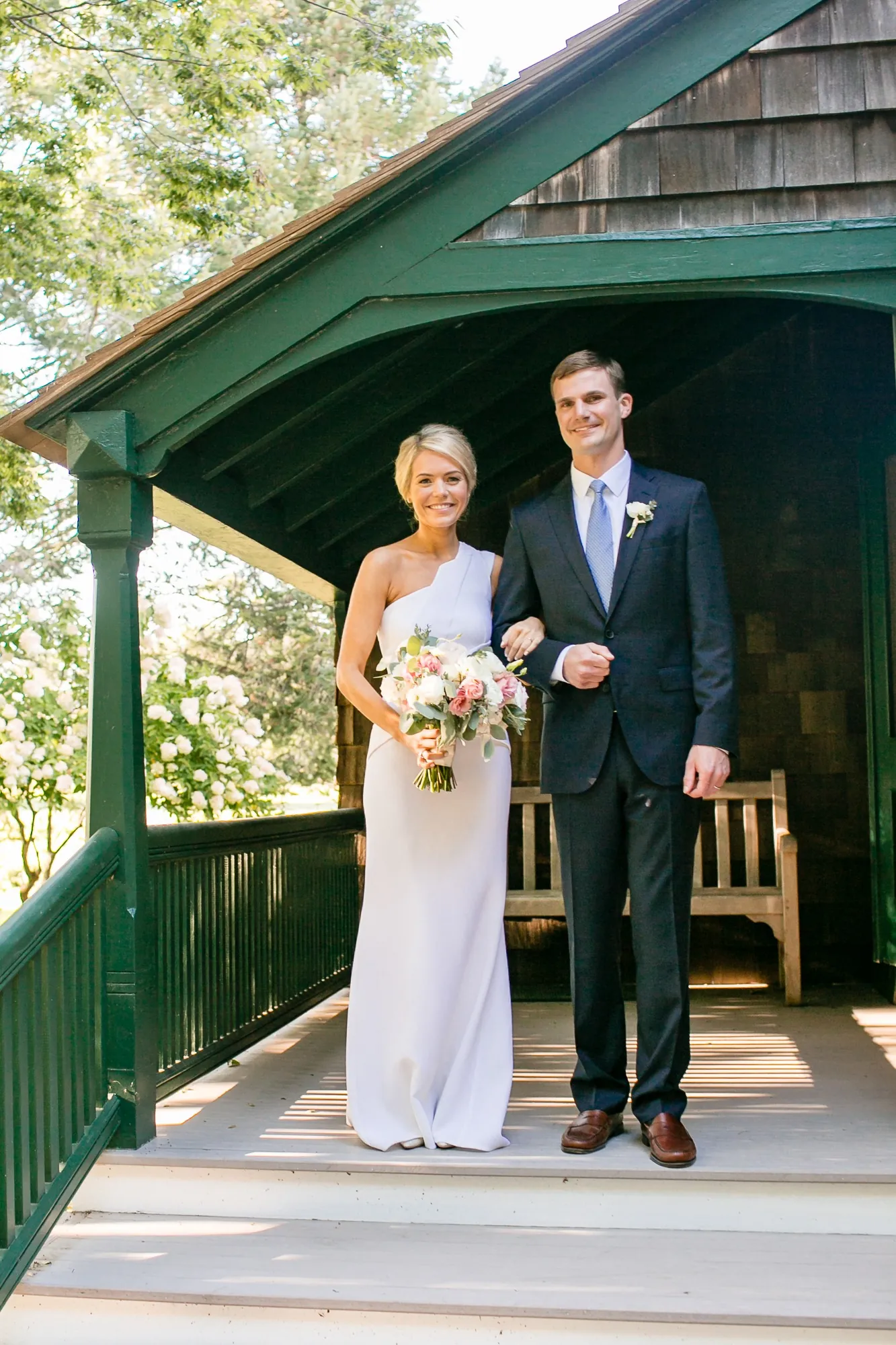 Kristen and Charlie stand arm in arm on the green-trimmed porch of the chapel