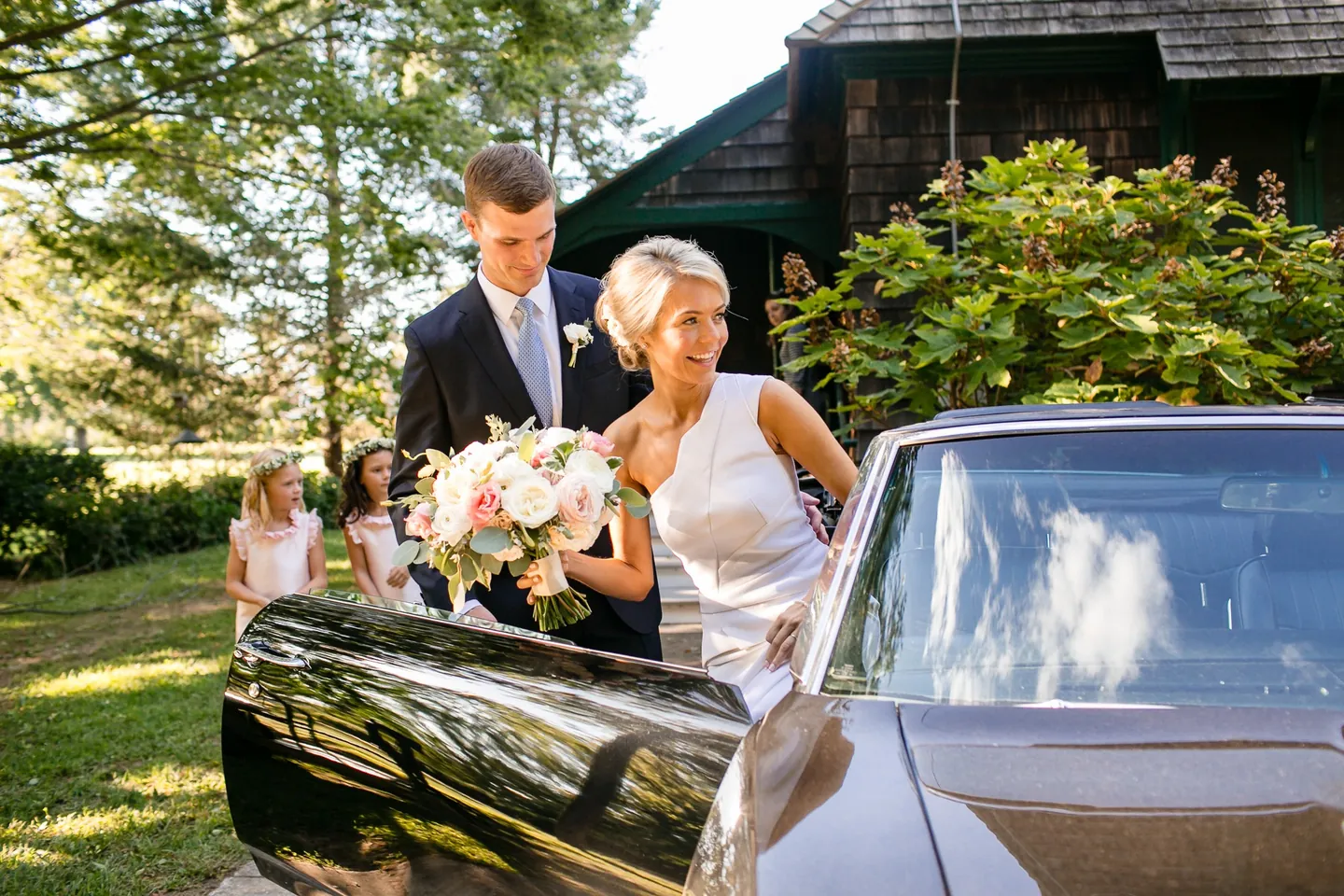 Charlie opens the convertible door for Kristen as flower girls watch from the lawn