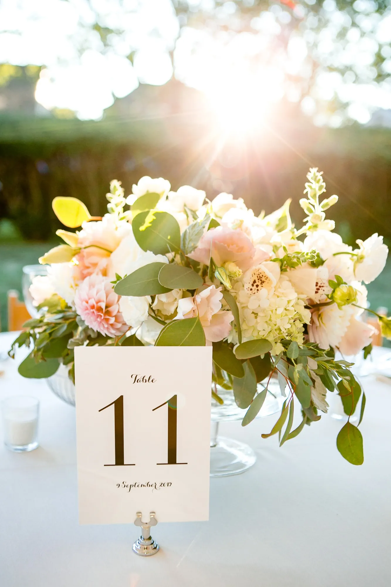 Table 11 card set in a low arrangement of blush roses and white flowers in soft backlight